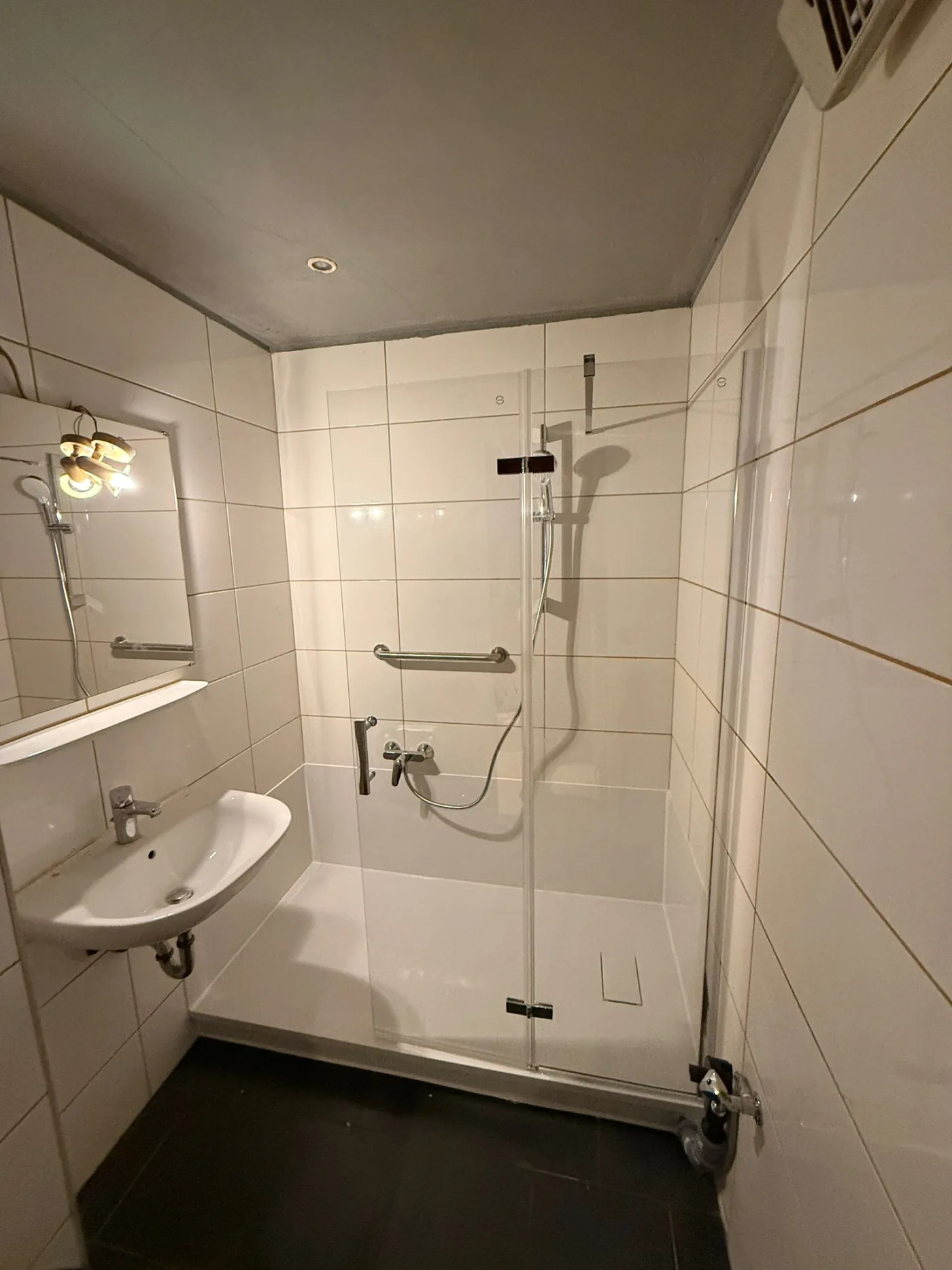 Kompakte Dusche mit dunklem Boden und Glasabtrennung